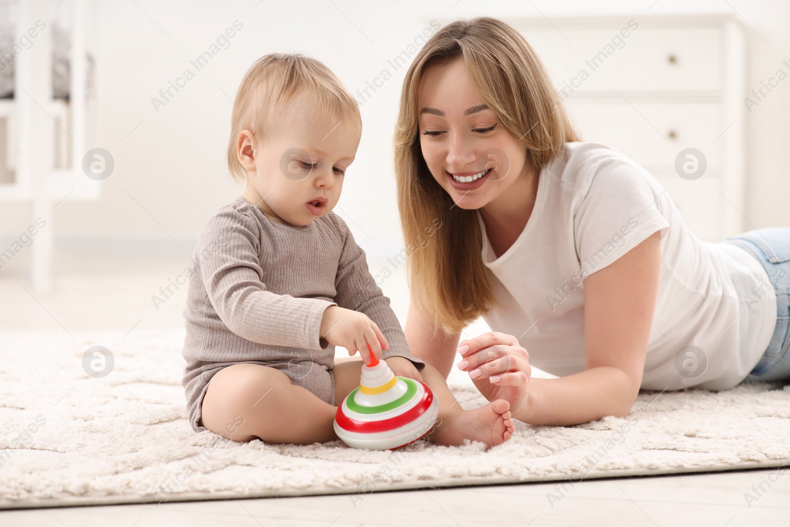 Photo of Children toys. Happy mother and her little son playing with spinning top on rug at home