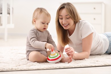 Photo of Children toys. Happy mother and her little son playing with spinning top on rug at home