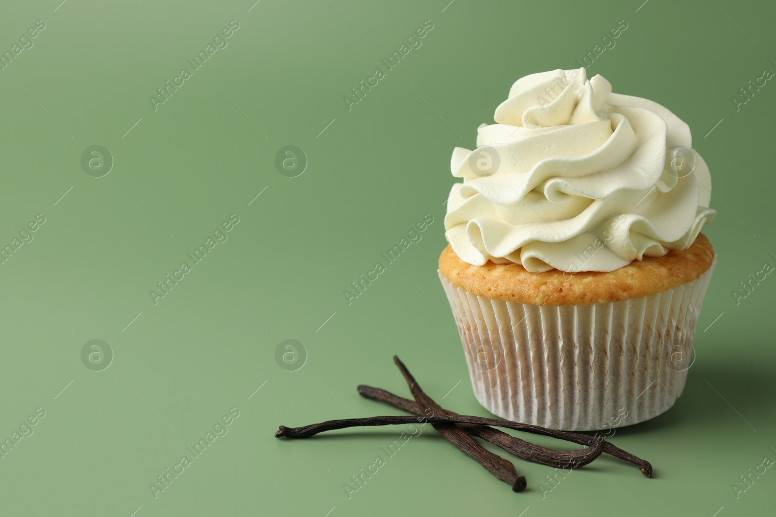 Photo of Tasty cupcake with cream and vanilla pods on green background, space for text