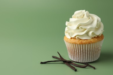 Tasty cupcake with cream and vanilla pods on green background, space for text