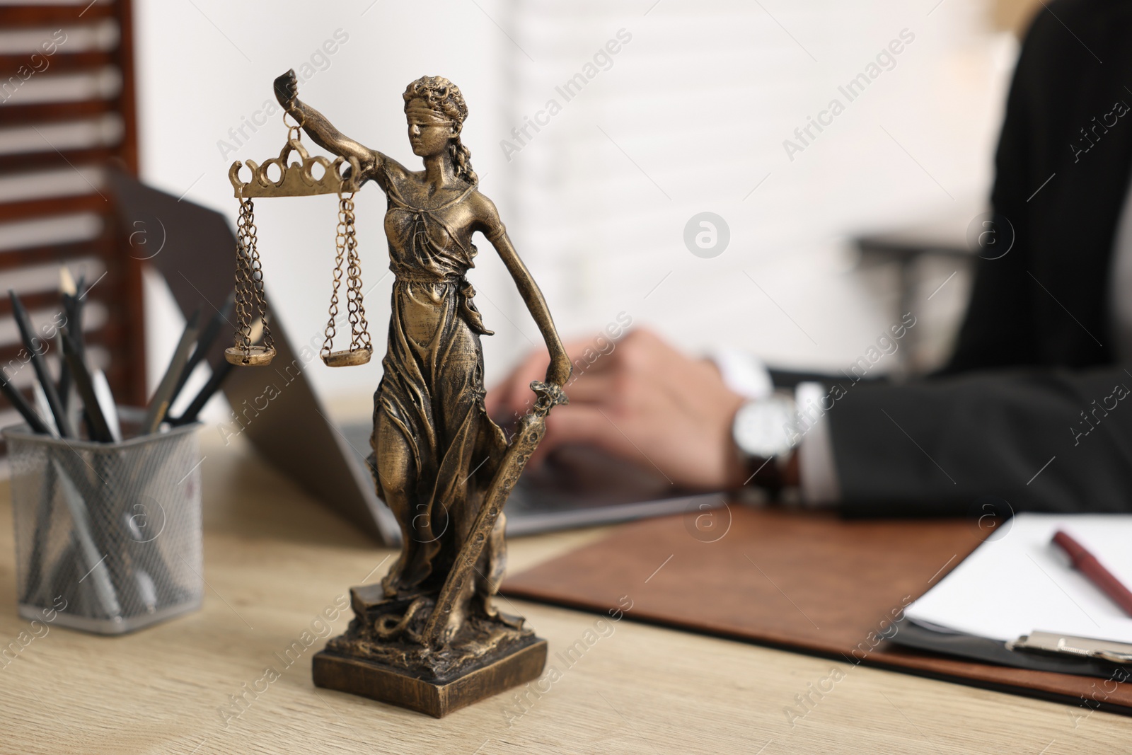 Photo of Lawyer working with laptop at table in office, focus on statue of Lady Justice