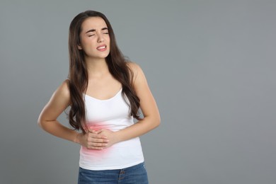 Young woman suffering from liver pain on grey background