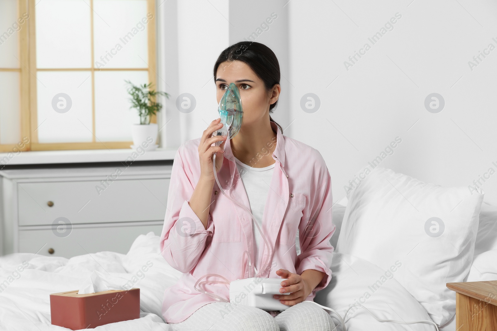 Photo of Sick young woman using nebulizer on bed at home