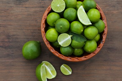 Photo of Whole and cut fresh ripe limes in bowl on wooden table, flat lay