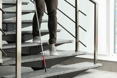 Blind person with long cane going down stairs indoors, closeup