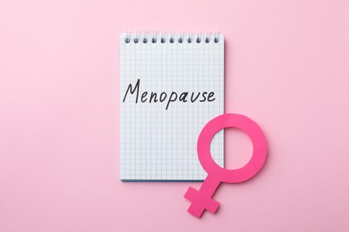 Notebook with word Menopause and female gender sign on pink background, top view