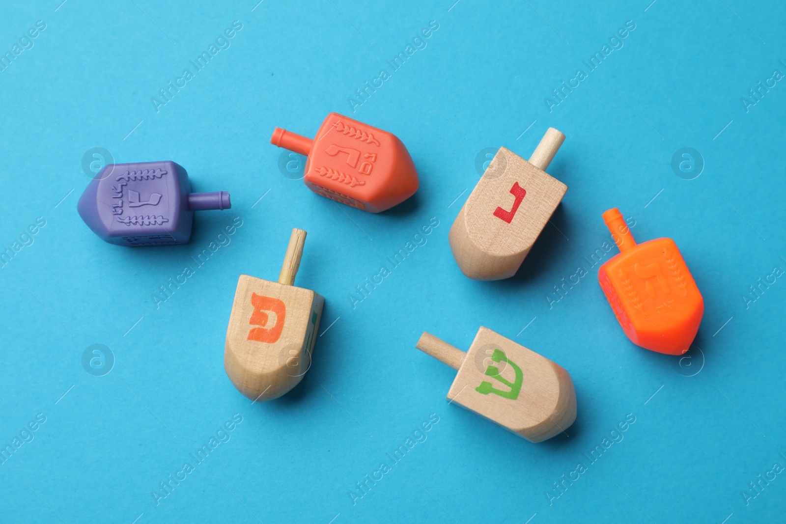 Photo of Different dreidels on light blue background, flat lay. Traditional Hanukkah game