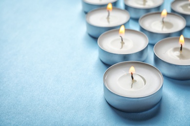 Photo of Small wax candles burning on color background, closeup