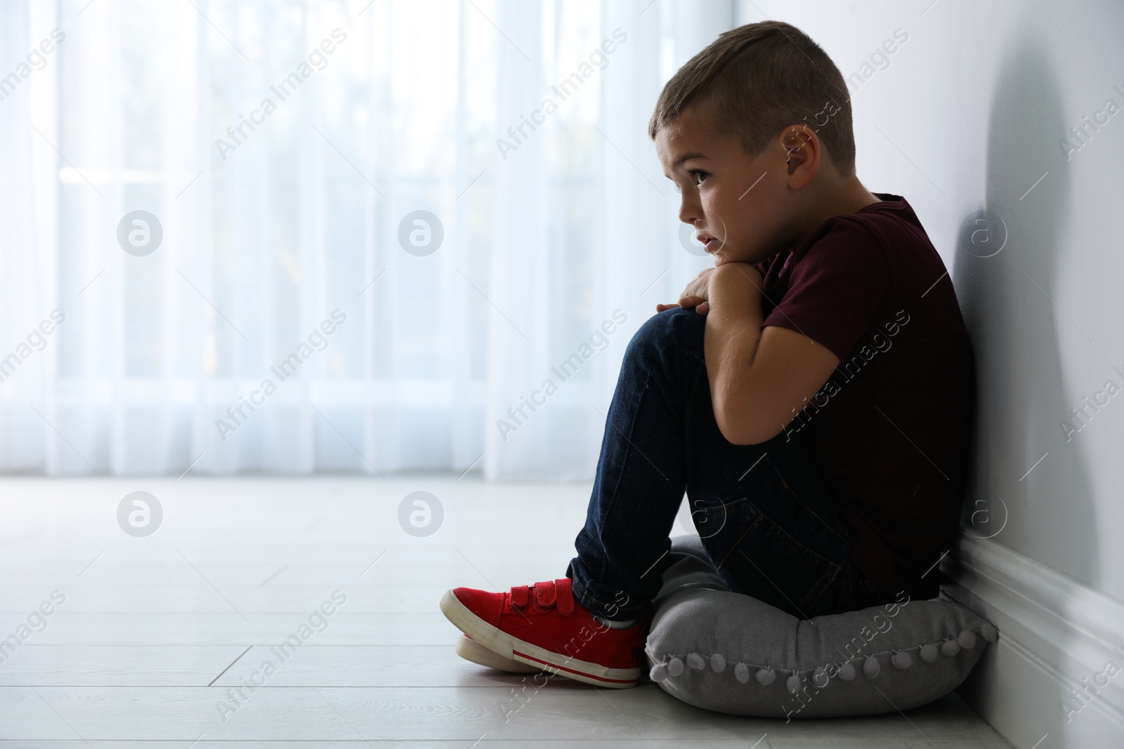 Photo of Sad little boy near white wall indoors, space for text. Domestic violence concept