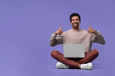 Photo of Smiling man with laptop showing thumbs up on purple background. Space for text