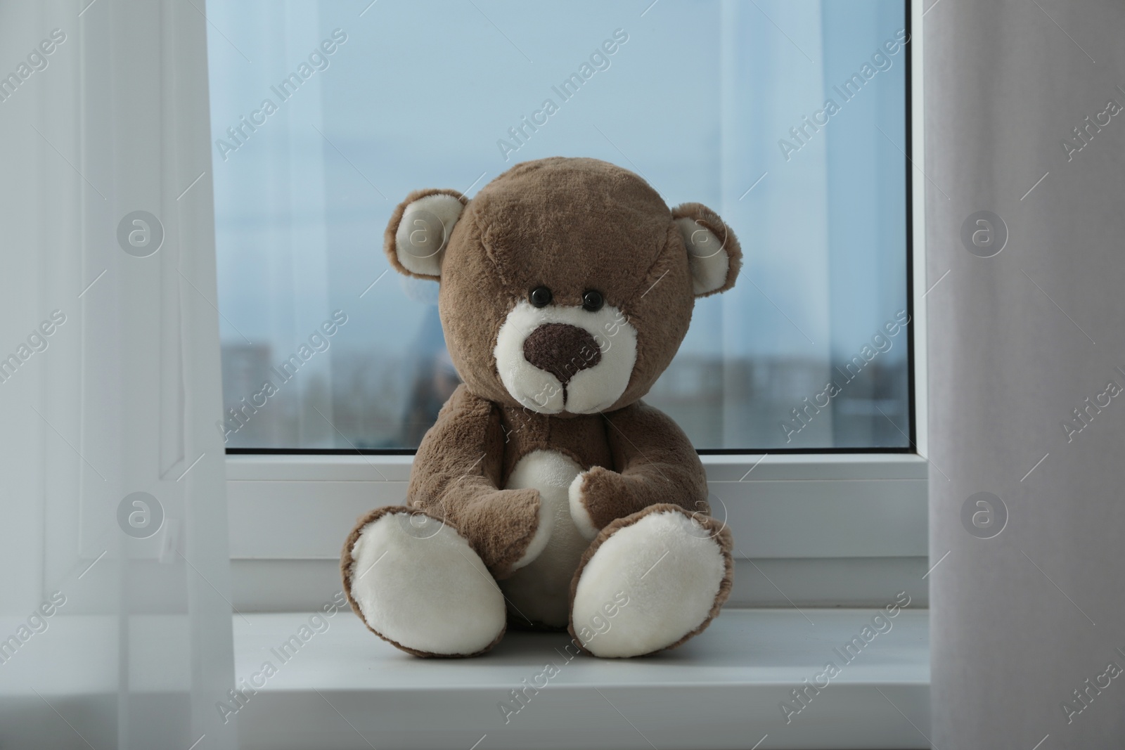 Photo of Cute lonely teddy bear on windowsill indoors