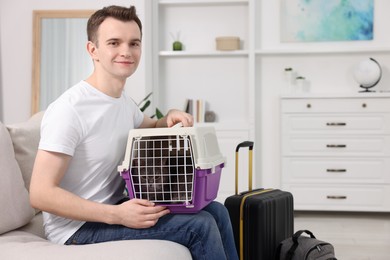 Photo of Travel with pet. Man holding carrier with cute cat on sofa at home, space for text