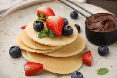 Delicious pancakes with berries and chocolate spread on plate, closeup