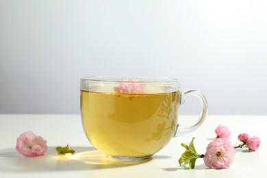 Photo of Glass cup of freshly brewed tea and beautiful flowers on light table