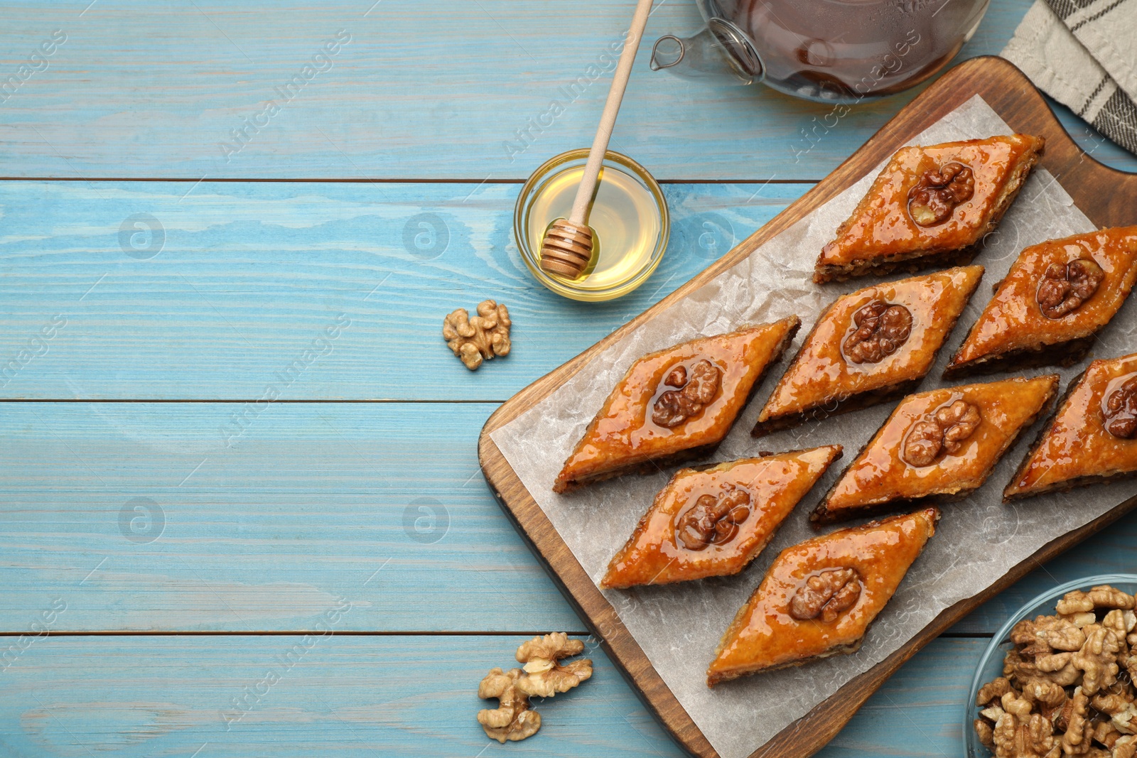 Photo of Delicious sweet baklava with walnuts and honey on turquoise wooden table, flat lay. Space for text