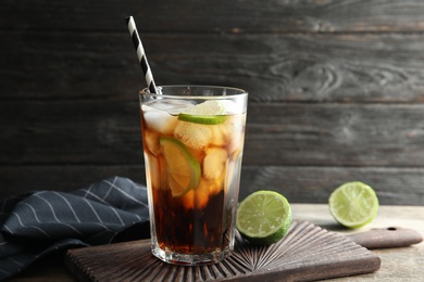 Photo of Glass of cocktail with cola, ice and cut lime on table