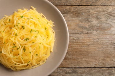 Plate of cooked spaghetti squash on wooden table, top view with space for text