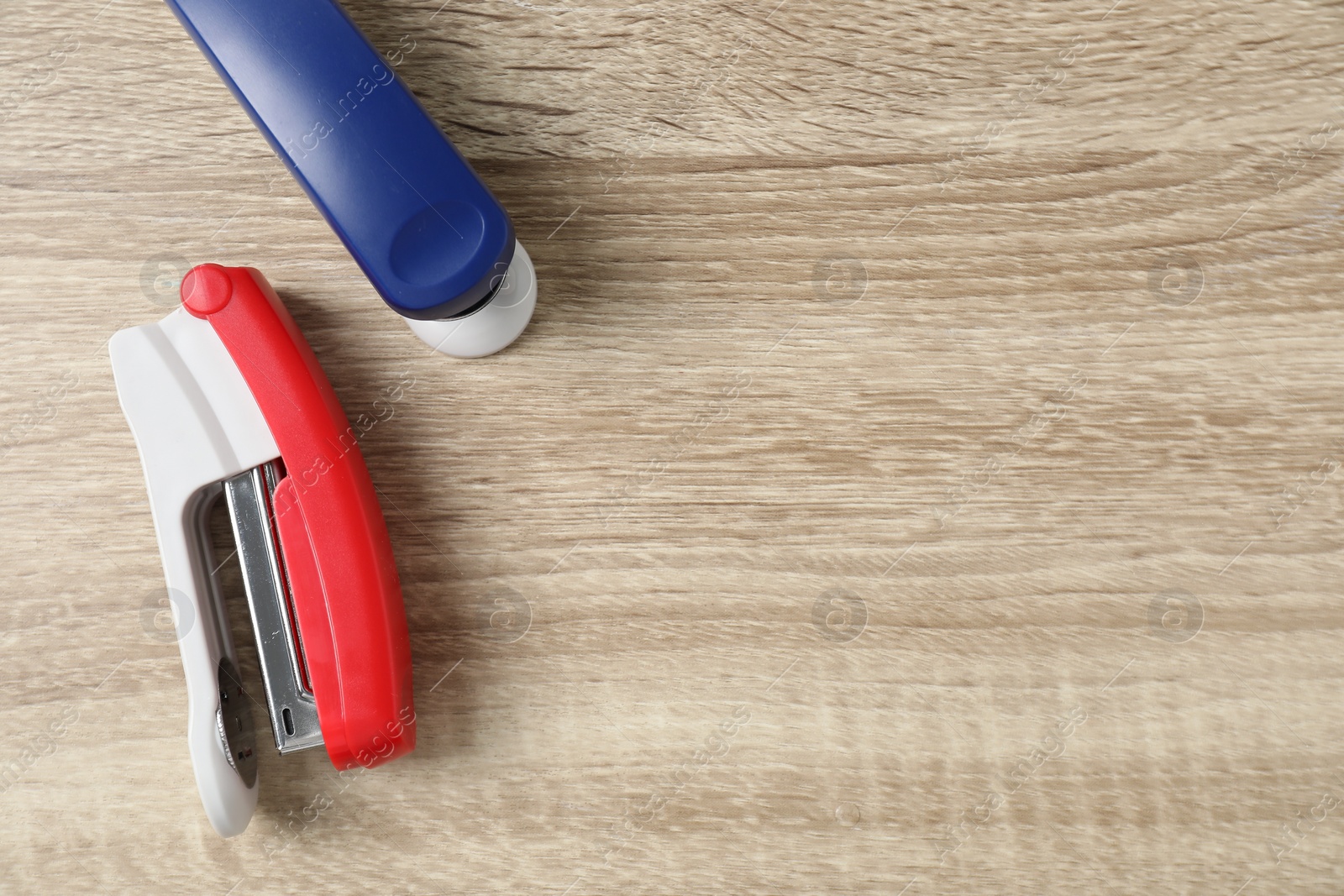 Photo of Color staplers on wooden table, flat lay. Space for text