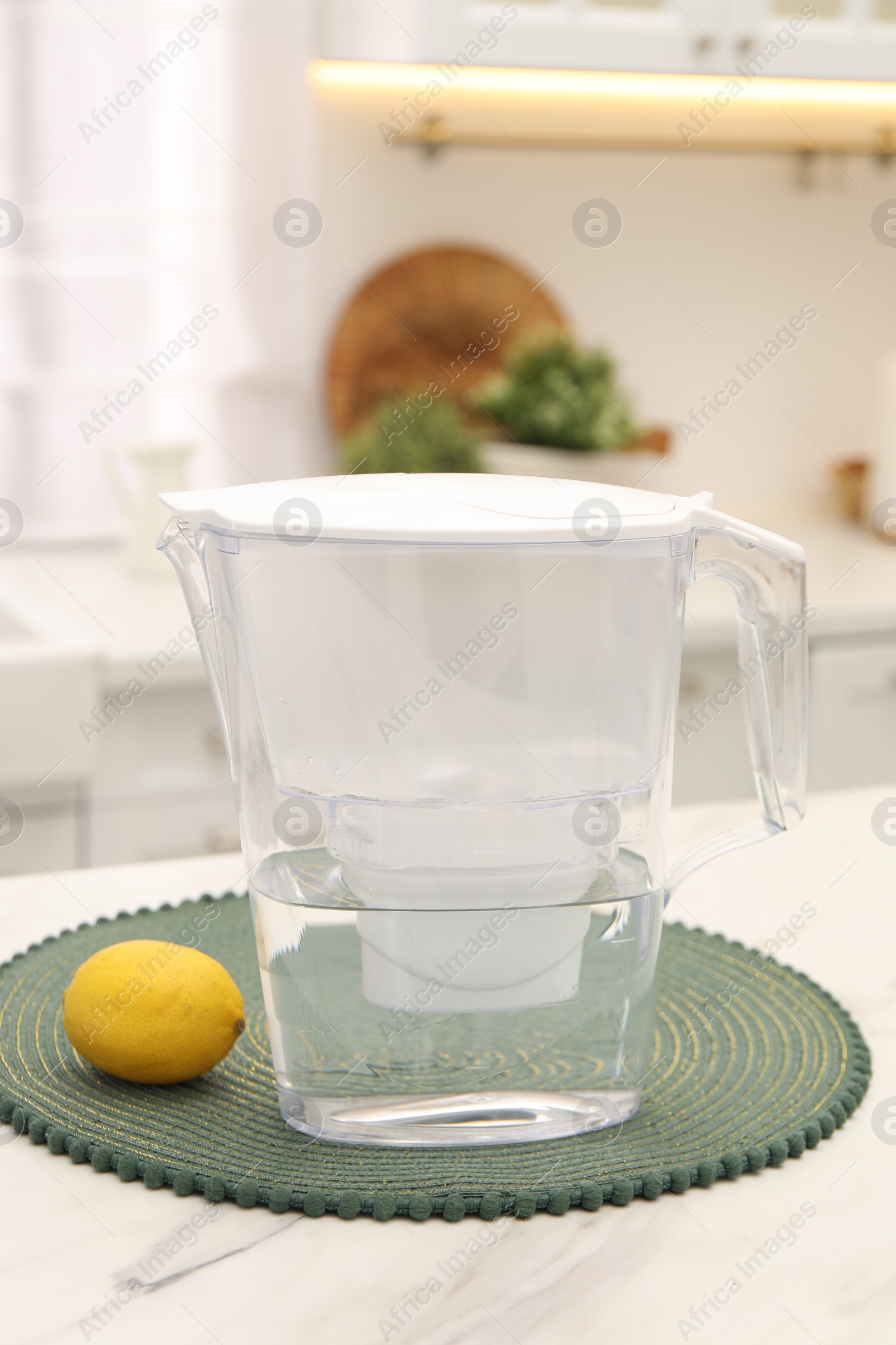 Photo of Water filter jug and lemon on white marble table in kitchen