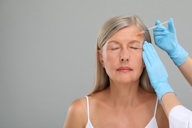 Photo of Doctor giving facial injection to senior woman on light grey background, closeup and space for text. Cosmetic surgery