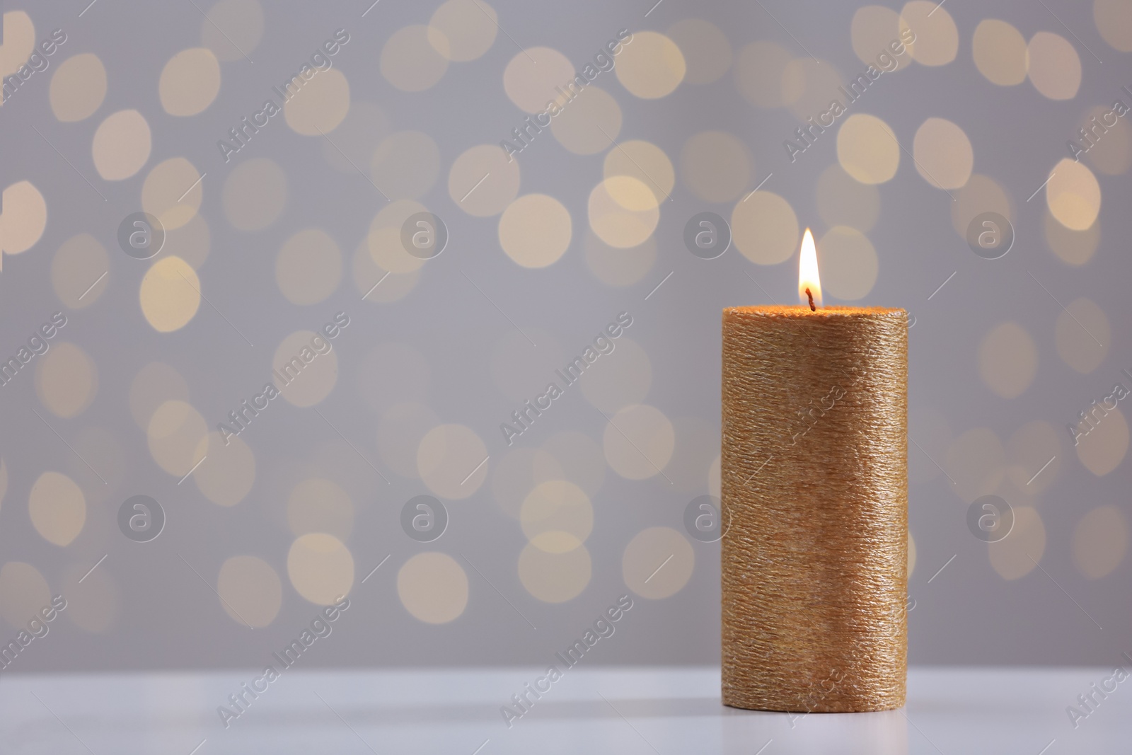 Photo of Burning gold candle on table against blurred lights. Space for text