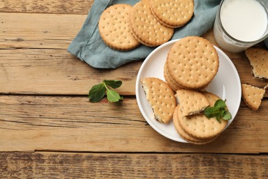 Tasty sandwich cookies and glass of milk on wooden table, flat lay. Space for text