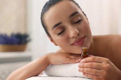 Beautiful young woman with bottle of essential oil on massage couch in spa salon
