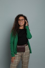 Beautiful African American woman with stylish waist bag on grey background