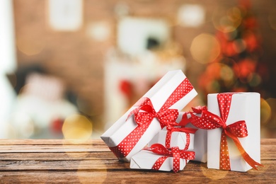 Image of Christmas gift boxes on wooden table in room, bokeh effect. Space for text