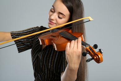Photo of Beautiful woman playing violin on grey background, focus on hand