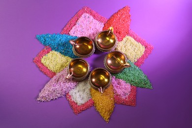 Photo of Diwali celebration. Diya lamps and colorful rangoli on purple background, flat lay