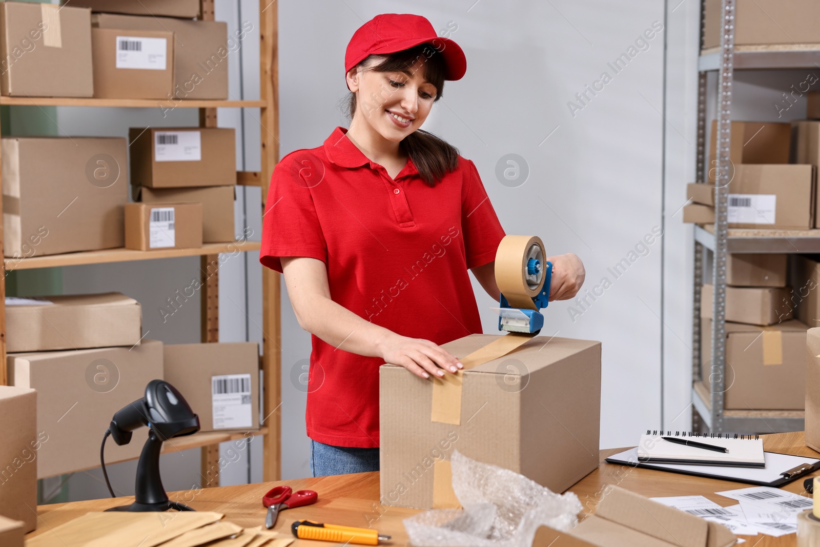 Photo of Parcel packing. Post office worker taping box at wooden table indoors