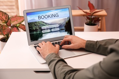 Man with laptop booking tickets online at white table, closeup. Travel agency concept