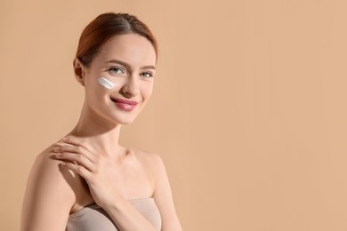 Beautiful young woman with sun protection cream on her face against beige background, space for text