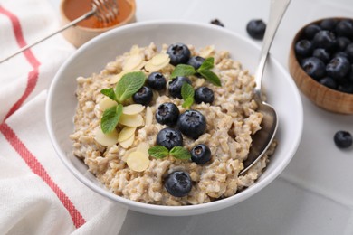 Photo of Tasty oatmeal with blueberries, mint and almond petals in bowl on white tiled table, closeup