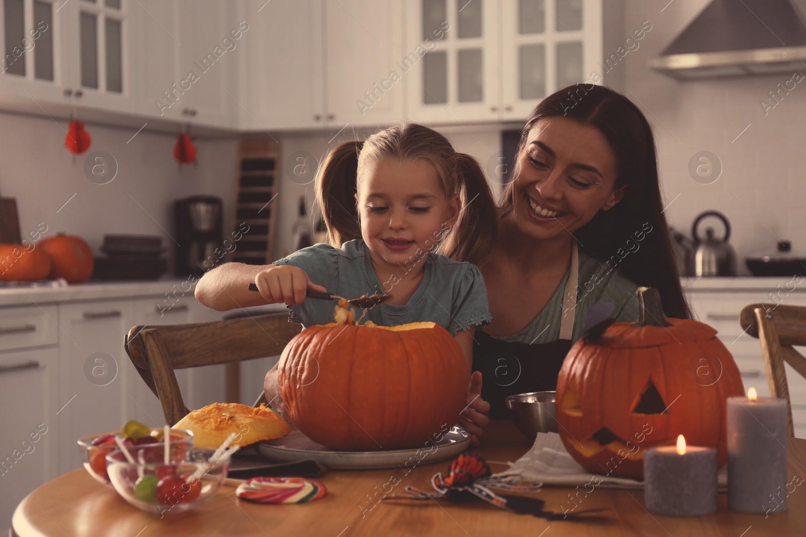 Photo of Mother and daughter making pumpkin jack o'lantern at table in kitchen. Halloween celebration