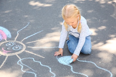 Photo of Little child drawing with colorful chalk on asphalt