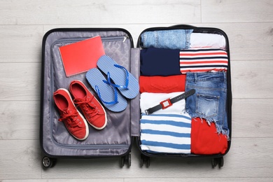 Photo of Packed suitcase with stuff on wooden background, top view