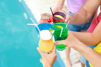 Friends clinking glasses with fresh summer cocktails near swimming pool, closeup