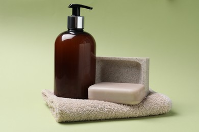 Photo of Soap bar, bottle dispenser and towel on green background