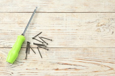 Photo of Screwdriver with green handle and screws on wooden table, flat lay. Space for text