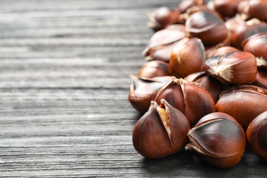 Photo of Delicious roasted edible chestnuts on black wooden table, closeup. Space for text