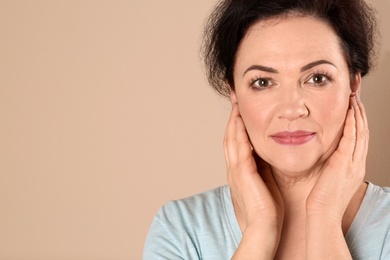 Photo of Portrait of charming mature woman with healthy beautiful face skin and natural makeup on beige background, closeup. Space for text