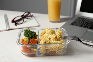 Container with tasty food, laptop, fork and glasses on white wooden table. Business lunch