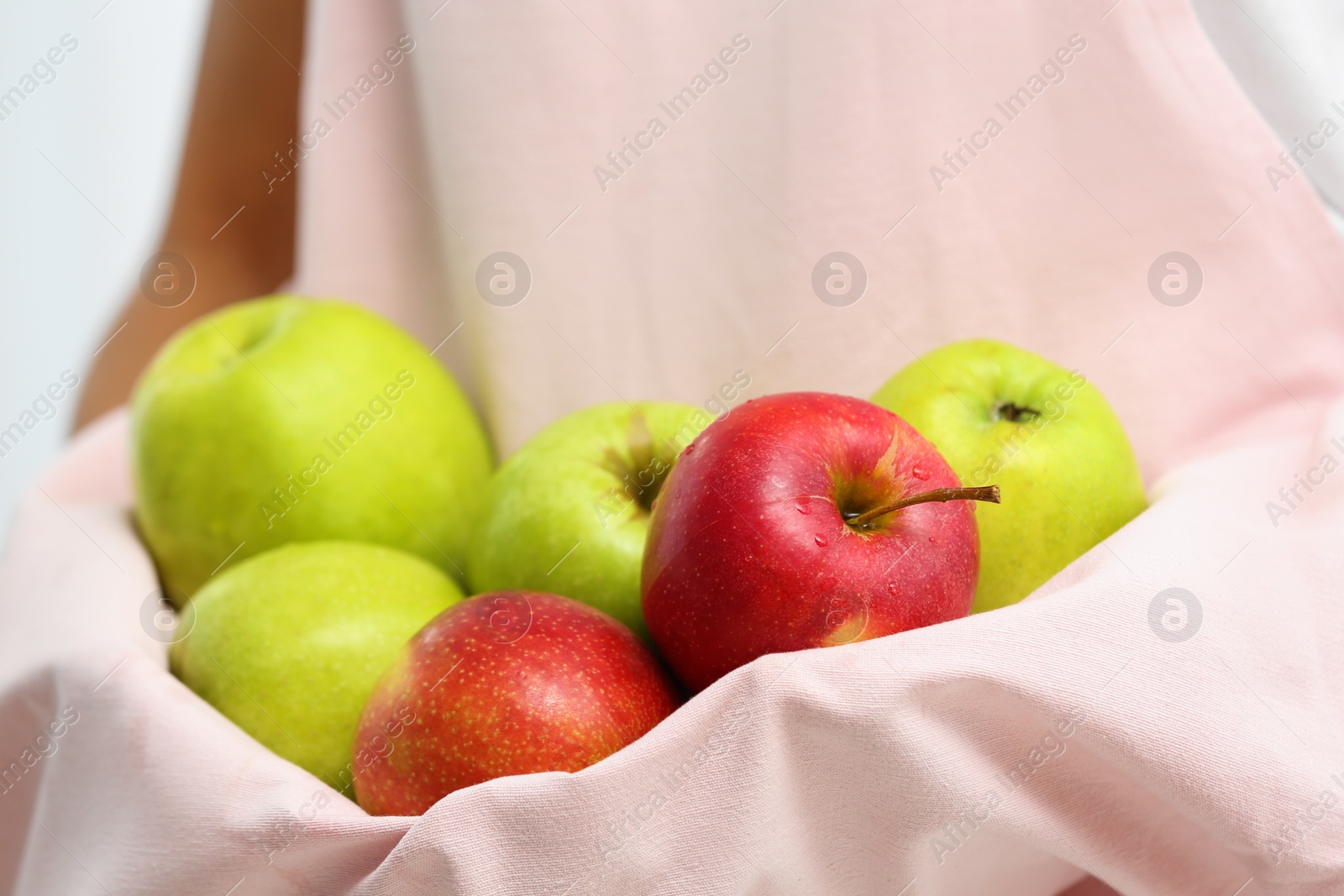 Photo of Woman holding pile of apples with hem of apron, closeup