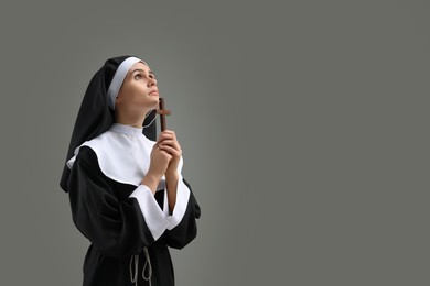 Photo of Nun with cross praying to God on grey background. Space for text