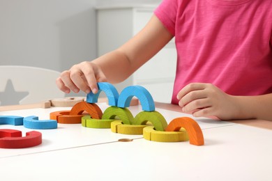 Photo of Motor skills development. Girl playing with colorful wooden arcs at white table indoors, closeup