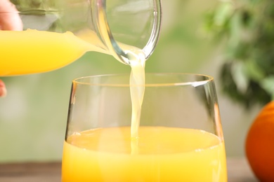Photo of Pouring fresh orange juice into glass, closeup