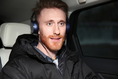 Young man listening to music with headphones in car. Space for text