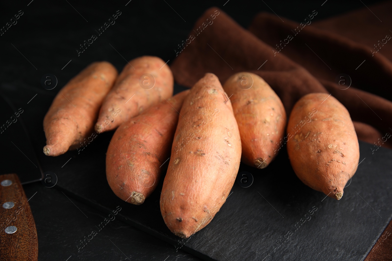 Photo of Heap of whole ripe sweet potatoes on black table